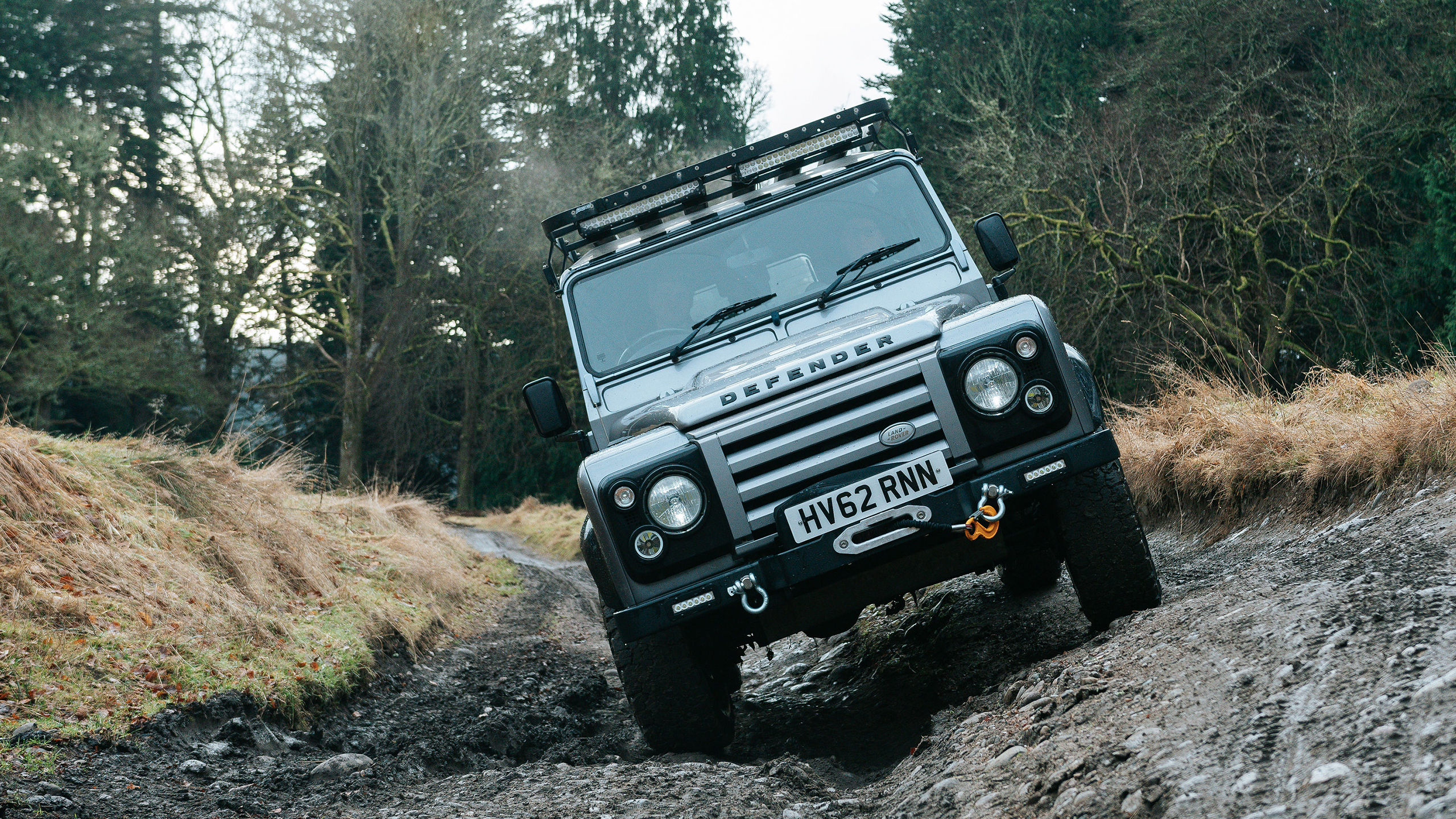 A grey Defender off-roading on a muddy forest track.